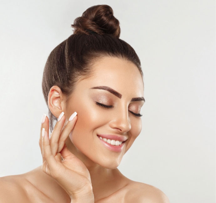 Lächelnde Frau mit Dutt mit Hand an Gesicht steht für Skinbooster